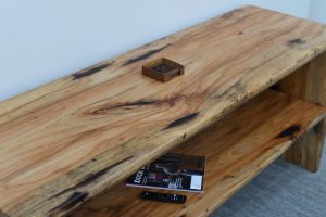Weathered wooden workbench with a small brown container on top and magazines plus two remote controls on the lower shelf nearby.