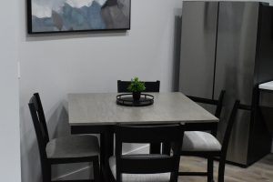 Modern dining table with dark chairs and a small potted plant centerpiece in a gray-walled room.