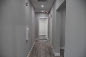 Gray interior hallway with white doors at the far end, wood-look flooring and overhead lights.