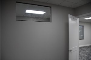 Grey interior wall with a partially open white door revealing an office space with a window.