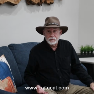 Older man with a brown hat and white beard seated on a blue couch in a living room.